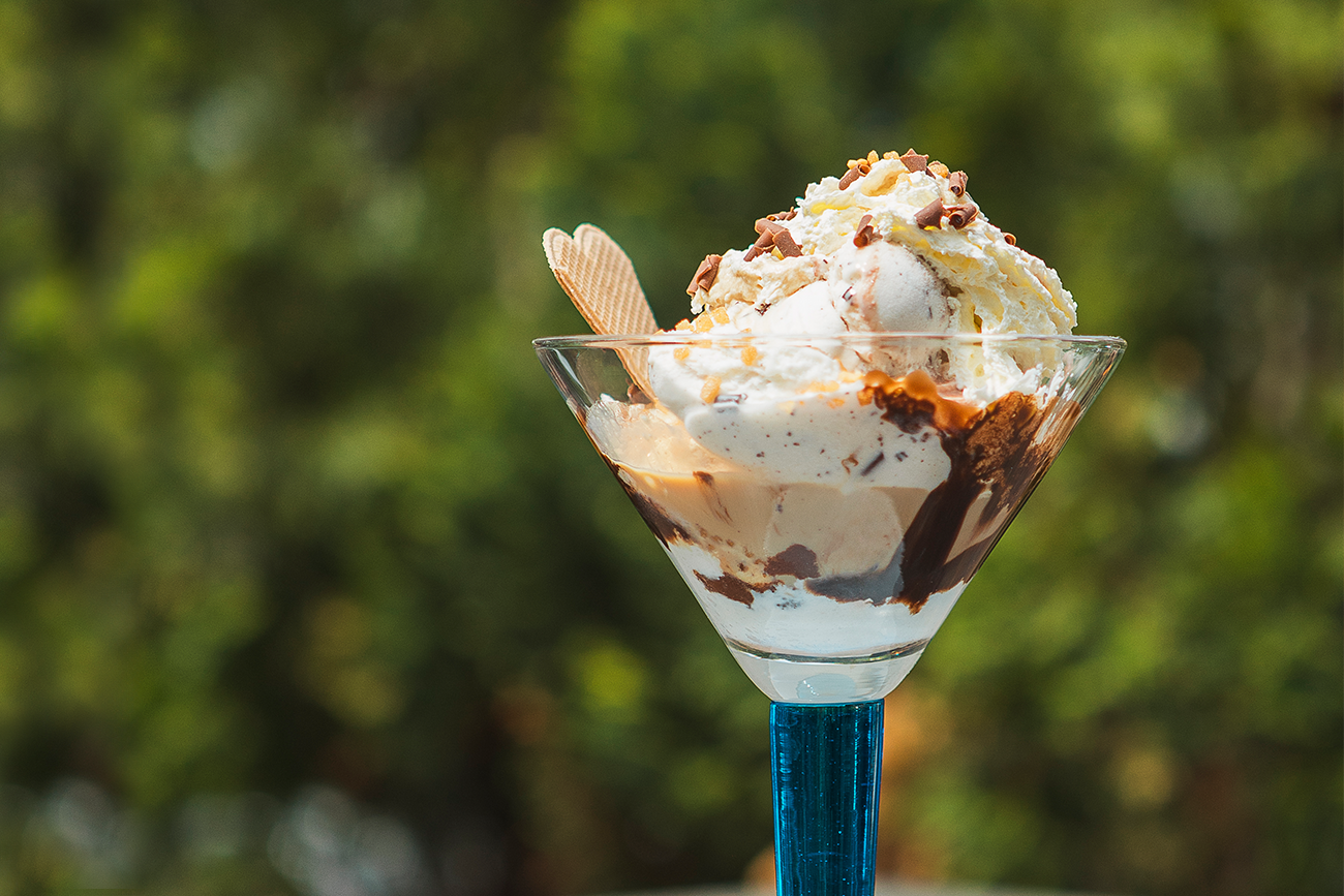 Baileysbecher mit Sahnehaube, Schokoladenraspeln und Waffel. Der Becher wurde draußen serviert und wird vom Sonnenlicht angestrahlt.