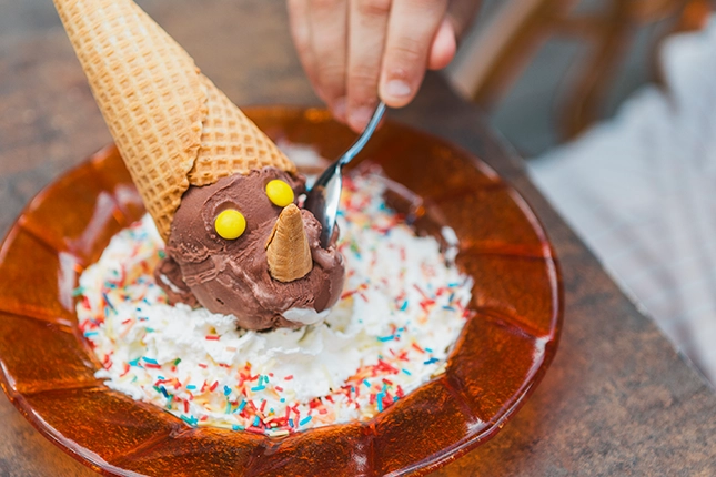 Junge Kundin, die unseren Pinocchiobecher für unsere kleinen Gäste probiert. Das Eis hat die Form von Pinocchio, was daran zu erkennen ist, dass der Kopf in Form der Eiskugel ein Hörnchen trägt, die lange Nase aus einem kleinen Hörnchen und die Augen aus Smarties bestehen.