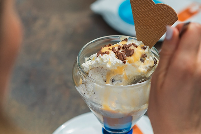 Eierlikörbecher mit Eierlikör, Schokoladenstreuseln und Waffel, die von einer Kunden verzehrt werden.