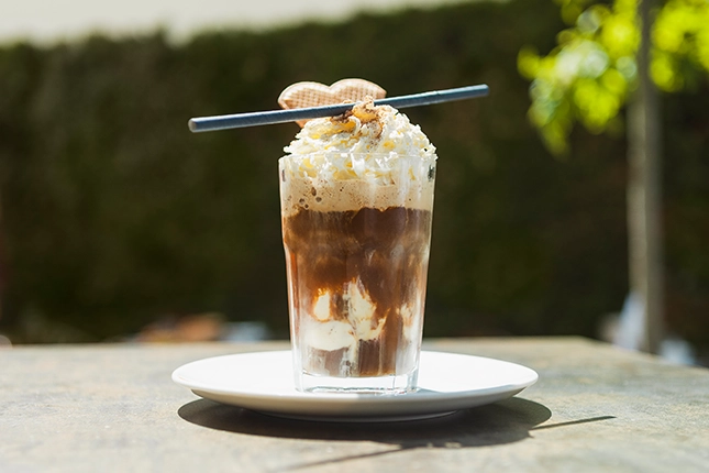 Kalter Eiskaffee mit Sahnehaube, Waffel und Strohhalm serviert – die perfekte kühle Erfrischung im Sommer für unsere Kaffeeliebhaber.