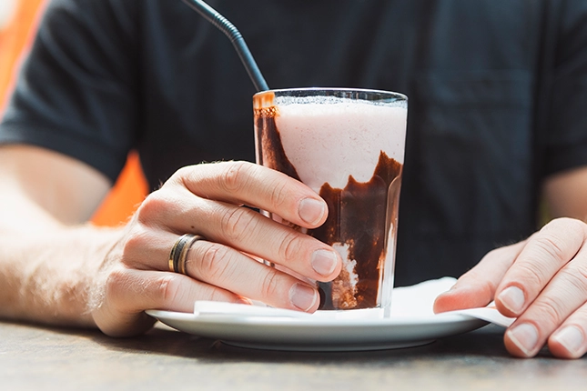 Erdbeermilchshake der Bäckerei Müller, der von den Händen eines Mannes umschlossen wird.