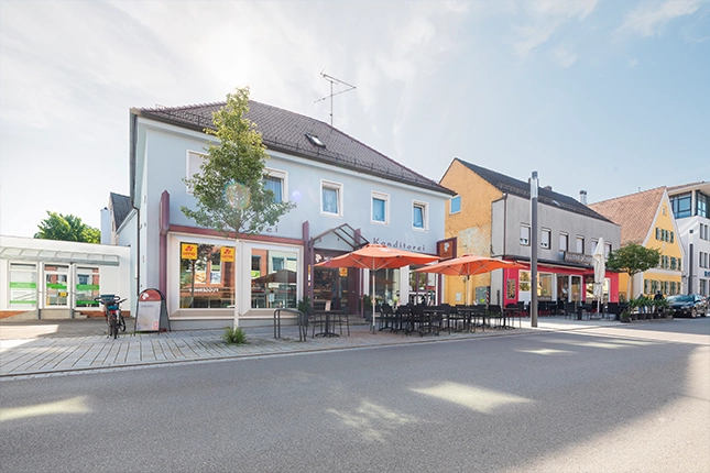 Außenaufnahme der Filiale in der Fuggerstraße in Schwabmünchen. Am Bordstein sind Sonnenschirme und der bestuhlte Außenbereich zu erkennen.