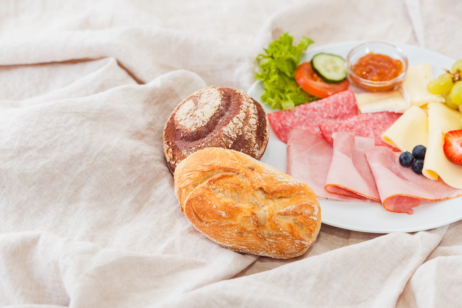 Frühstücksteller des klassischen Frühstücks mit Schinken, Salami, Käse, Butter, Marmelade, Salat, Gurke, Tomate, Blaubeeren, Erdbeeren und zwei Semmeln.