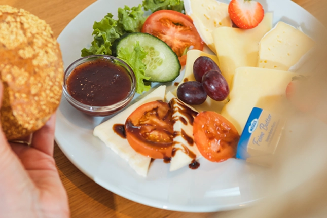 Nahaufnahme unseres Käse-Frühstücks, bestehend aus einer Käsevariation, Tomate-Mozzarella-Salat, Butter, Marmelade, Brotkörbchen, Salat, Tomate und Gurke.