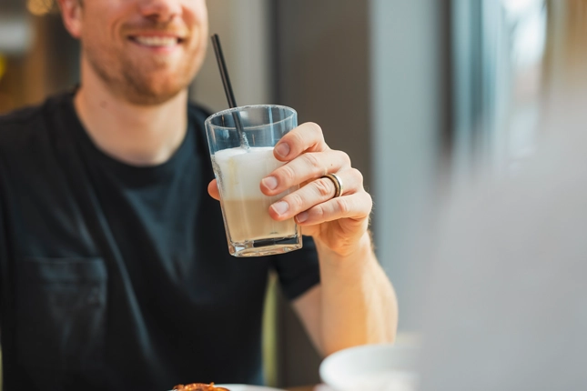 Männlicher Gast der einen Latte Macchiato in der Hand hält.