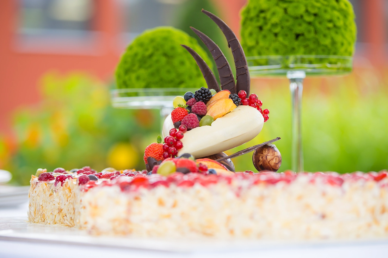 Detailaufnahme eines Hochzeitstortentoppers in Herzform aus weißer Schokolade. Das Herz ist mit Beeren und Früchten gefüllt und thront auf der Hochzeitstorte in doppelter Herzform