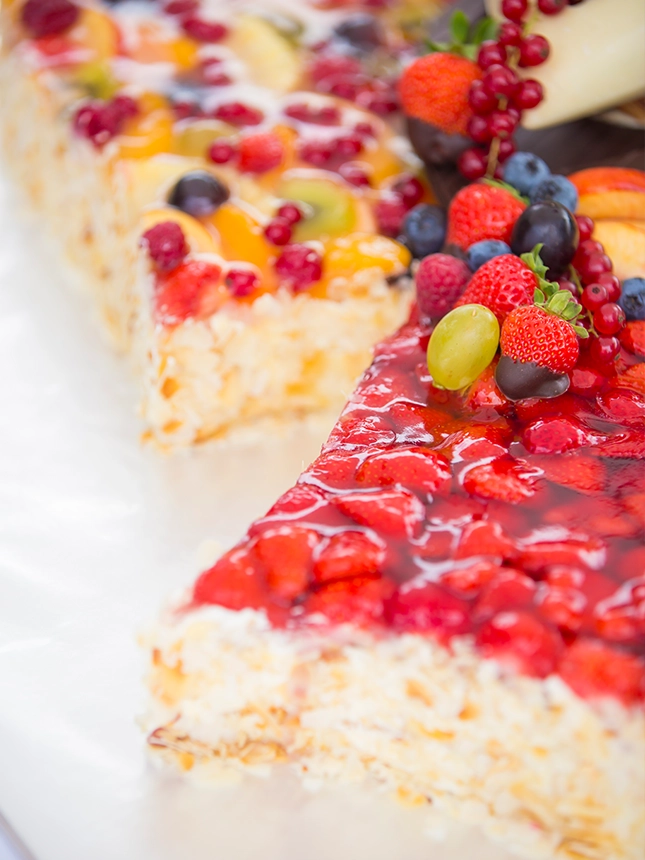 Detailaufnahme einer Hochzeitstorte in doppelter Herzform. Die Torte besteht aus luftigem Bisquitboden und die Herzen sind aufgeteilt in roten Erdbeerer- und bunten Früchtekuchen