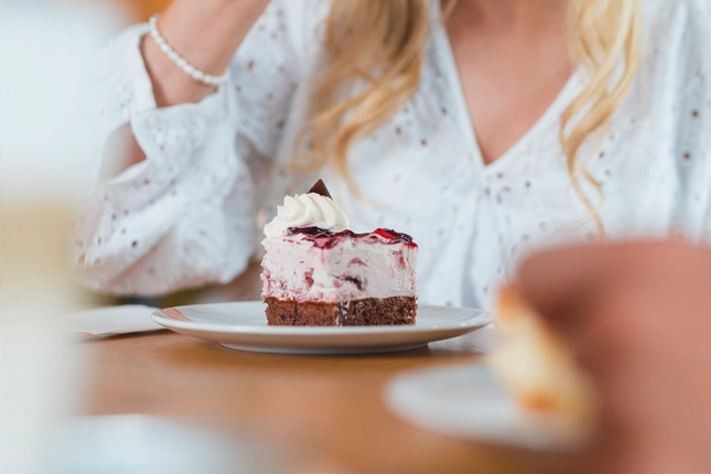 Nahaufnahme eines fruchtigen Kuchenstückchens mit Sahnehaube, das gerade von einem weiblichen Gast verzehrt wird.