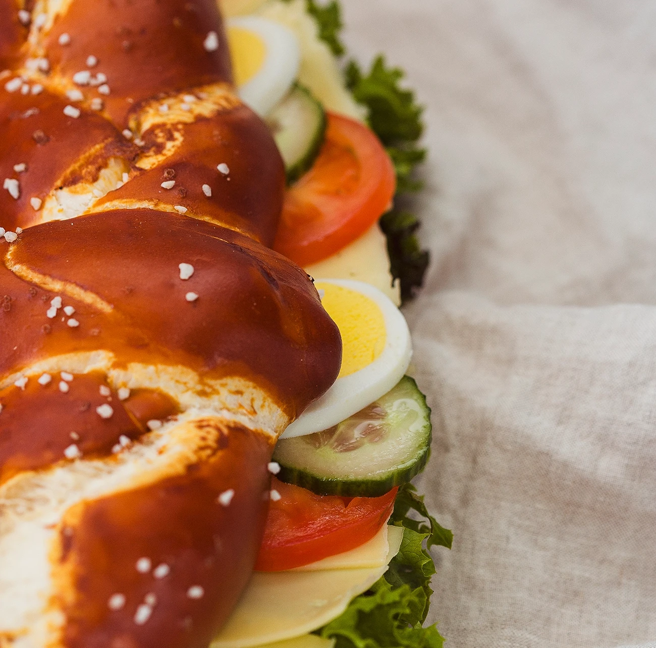 Nahaufnahme der großen belegten Partybreze mit Gurken, Tomaten, Salat, Käse und Ei auf Leinenstoff