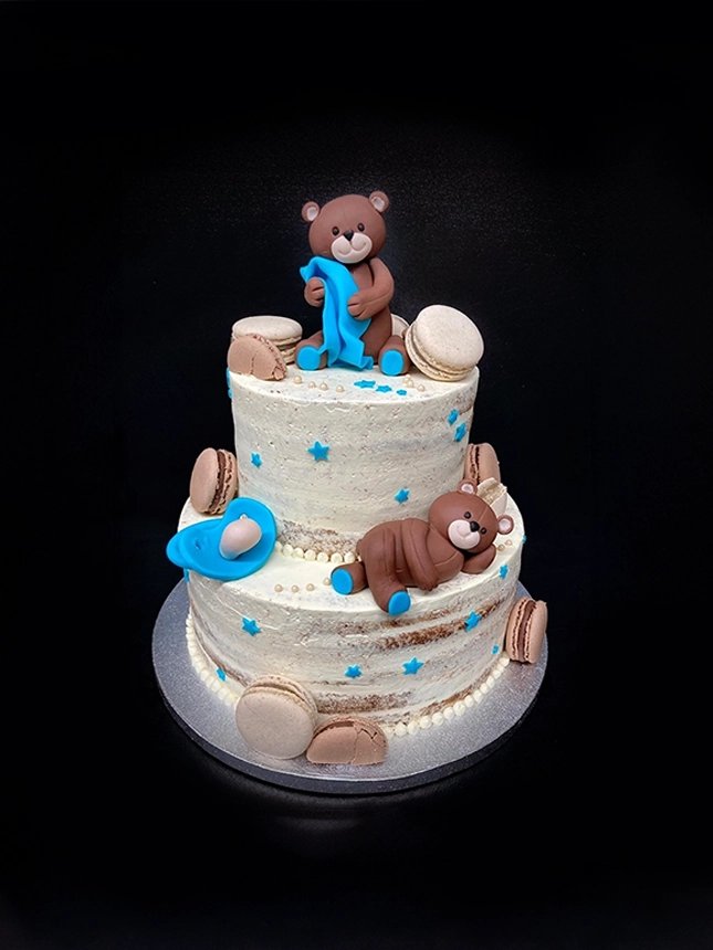 Torte zur Geburt oder Babyparty. Die Torte im Naget-Cake-Stil in Beige wird von Macarons, einem blauen Schnuller, blauen Sternen sowie zwei Teddybären geschmückt